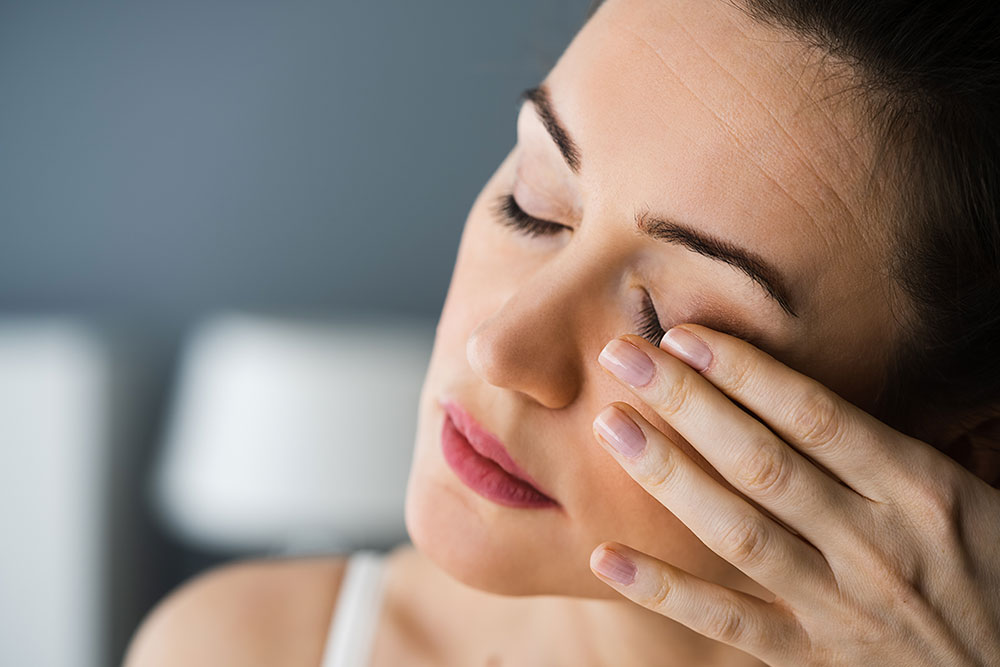 Frau mit geschlossenen Augen streicht mit einer Hand über das rechte Auge