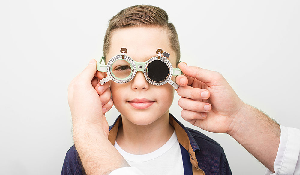 Junge wird mit einer optischen Messbrille untersucht und dabei ein Auge abgedeckt