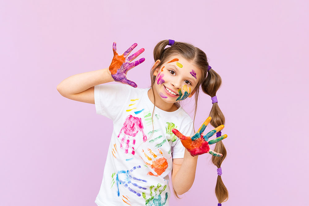 Mädchen mit Zopf, in Farbe getunkten Händen und T-Shirt mit Handabdrücken